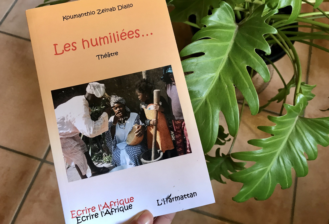 Guinean family outdoors in conversation on cover of book, held against plant